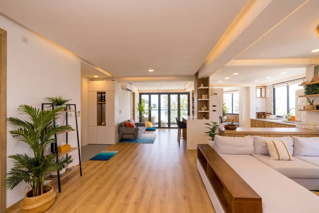 Long open-plan living area with timber floors, a potted palm and a low sofa leading to the windows