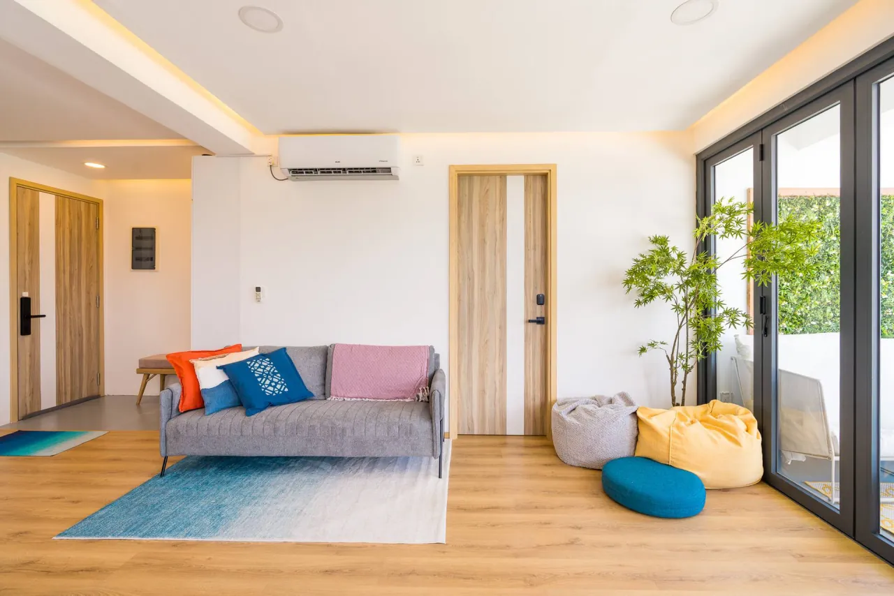 A grey sofa with colourful cushions, bean bags and a blue rug beside the balcony doors