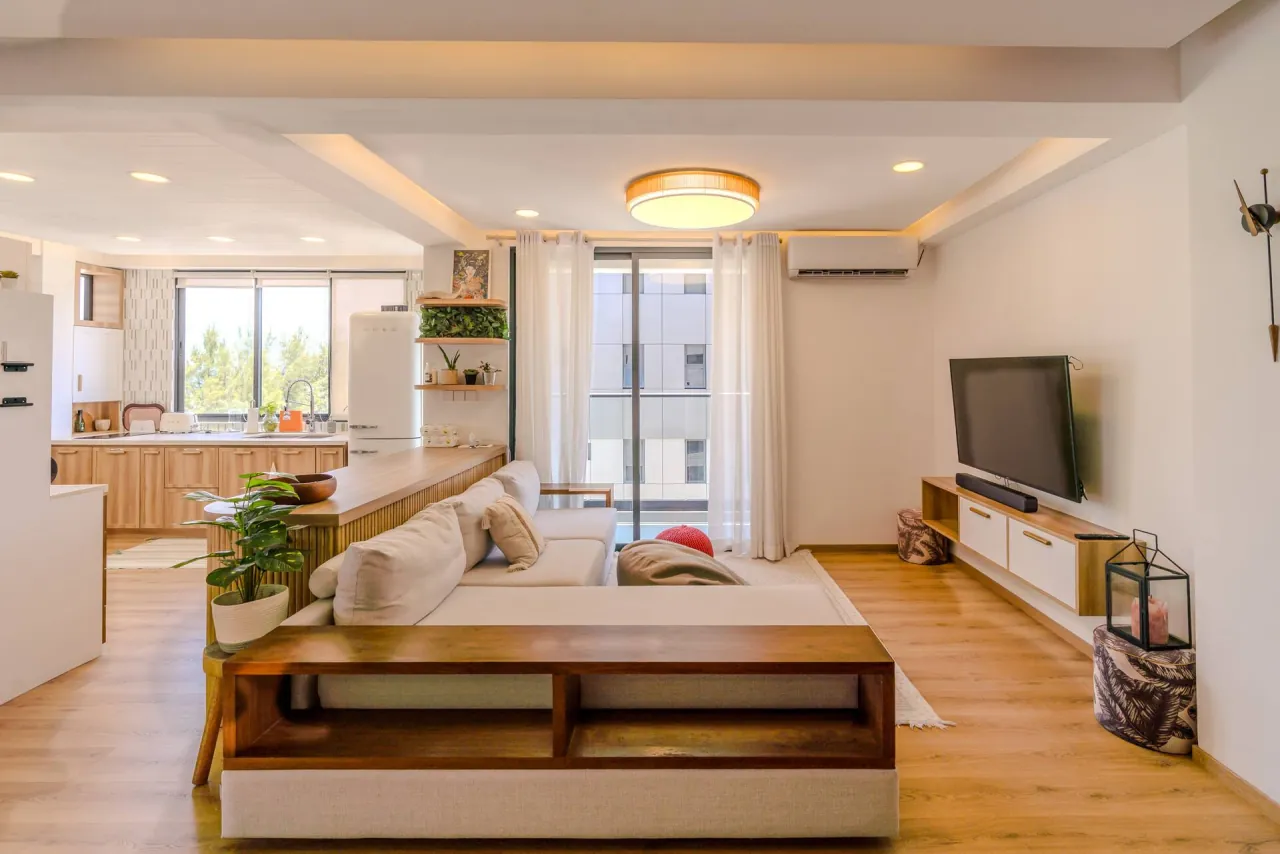 Sofa facing a wall-mounted TV, with the kitchen and windows behind