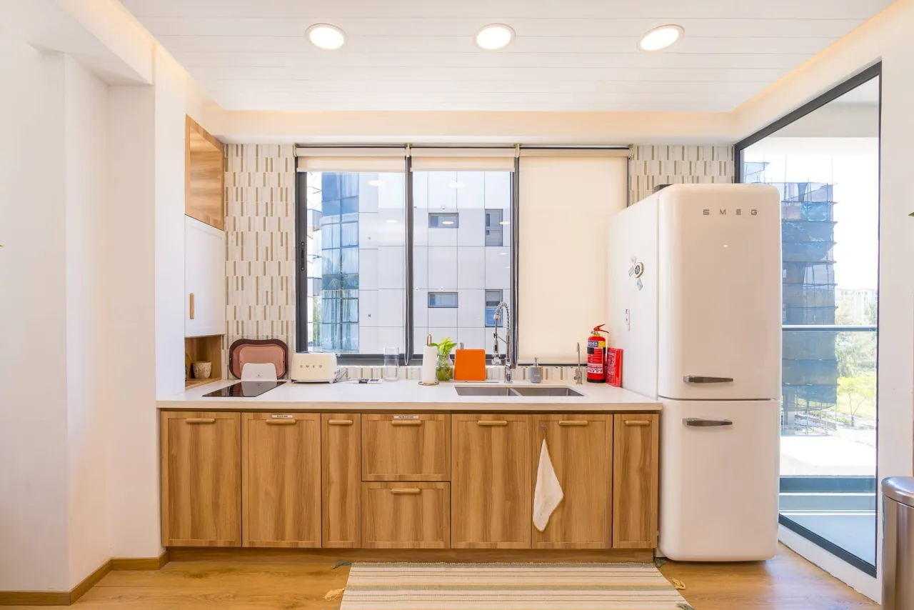 Timber kitchen counter with a sink and a cream retro fridge beside a window
