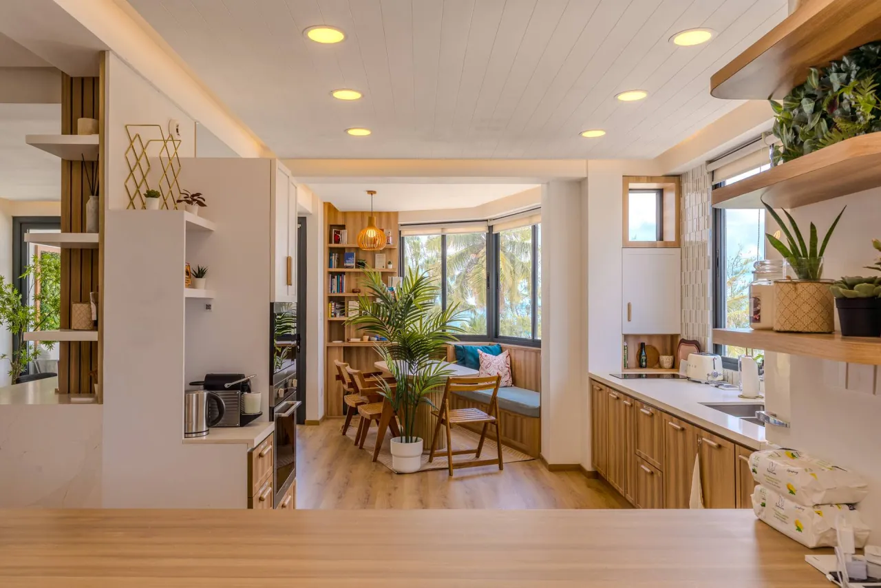 Dining table and chairs by windows full of palms, with open timber shelves