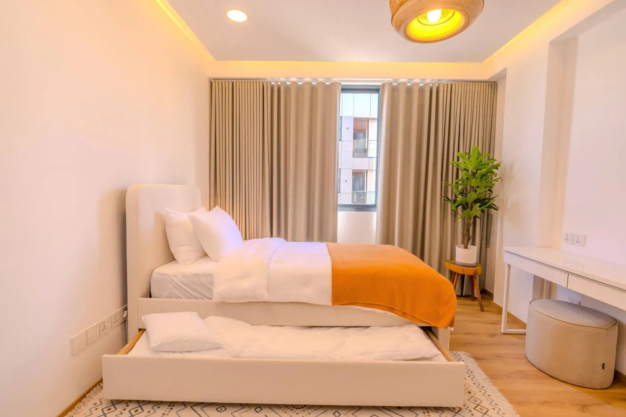 Single bed with an orange throw and a pull-out second bed beneath, beside a dressing table