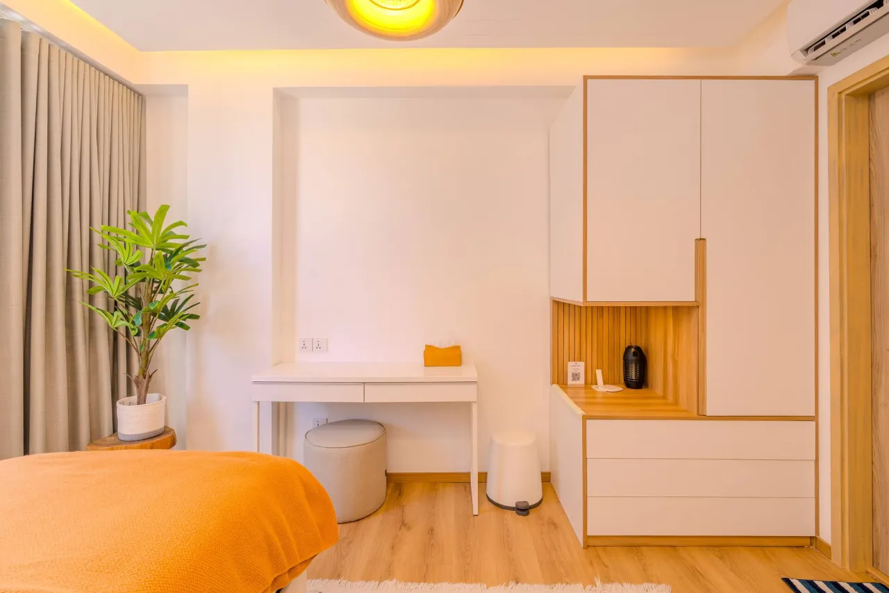 A desk, wardrobe and plant beside a bed with an orange throw