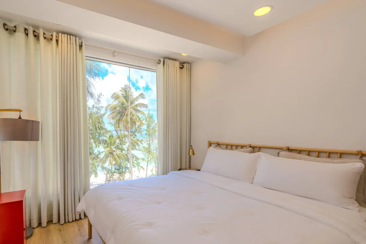 Super king bed with white linen beside a window looking out over palms to the ocean