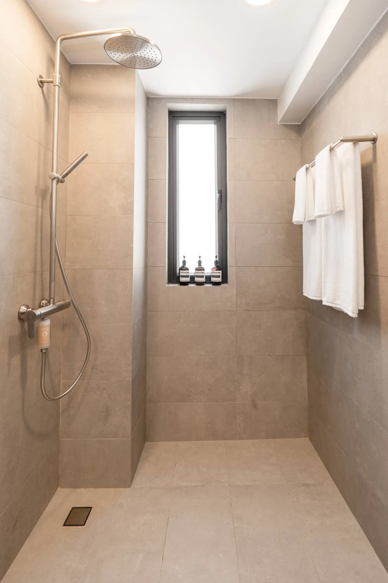 Grey-tiled walk-in shower with a rain showerhead and white towels