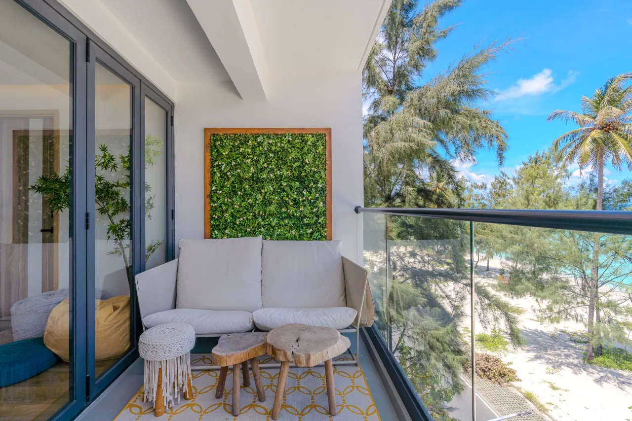 Balcony with a white sofa, stools and a green plant wall, looking over palms to the beach