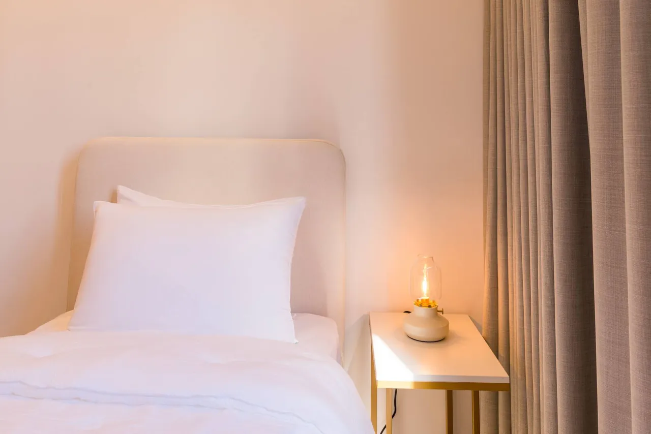Single bed with white linen beside a small lamp table